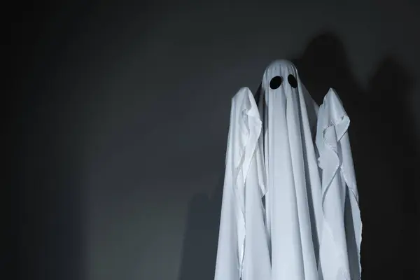 Creepy ghost. Woman covered by sheet against dark grey background, space for text