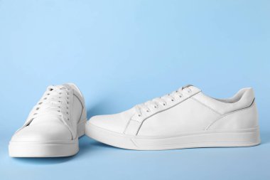 Açık mavi arka planda bir çift şık beyaz spor ayakkabı.