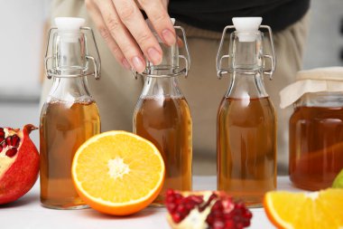 Beyaz masada mayalanmış bir şişe kombu çayı alan bir kadın.