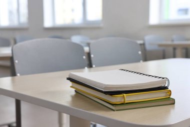 Boş sınıftaki ahşap masada yığınla defter var.