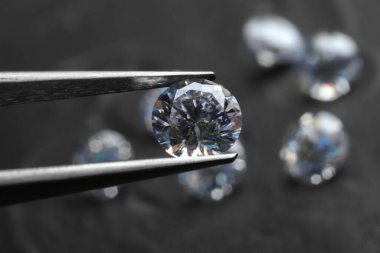 Cımbız, üzerinde parlak elmas olan koyu gri masa, yakın plan.