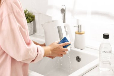 Mutfakta lavaboda elektrikli su ısıtıcısını süngerle yıkayan kadın.