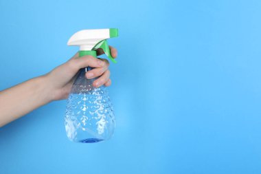 Açık mavi arka planda plastik sprey şişesi tutan kadın, yakın plan. Metin için boşluk