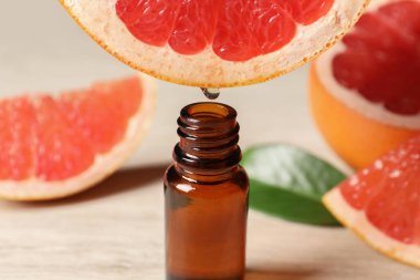 Temel yağ, arka planda hafif arkaplanda greyfurttan şişeye damlıyor.