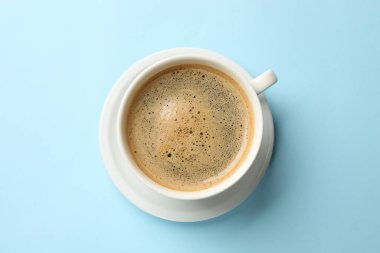 Açık mavi arka planda, fincanda koyu kahve, üst manzara.