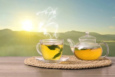 Cam bardakta yeşil çay ve dağlarda ahşap masada çaydanlık.