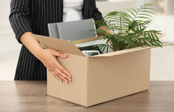 Unemployment problem. Woman with box of personal belongings at table in office, closeup