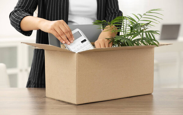 Unemployment problem. Woman with box of personal belongings at table in office, closeup
