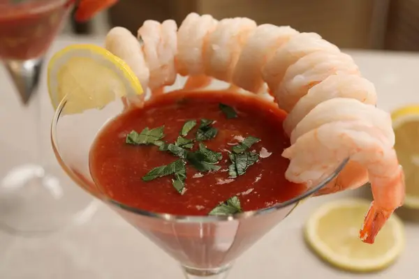 Tasty shrimp cocktail with sauce in glass and lemon on blurred background, closeup