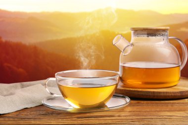 Cam bardakta yeşil çay ve dağlarda ahşap masada çaydanlık.