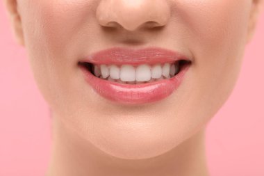 Temiz dişli kadın pembe arka planda gülümsüyor, yakın plan.