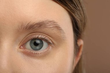 Açık kahverengi arka planda güzel doğal kirpikleri olan kadın, yakın plan.