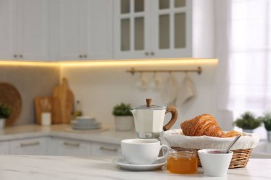 Kahvaltı mutfakta servis edilir. Taze kruvasan, reçel, bal ve kahve beyaz masada, mesaj için yer var.