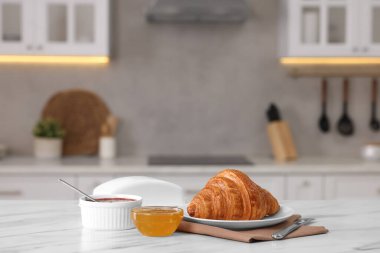 Kahvaltı mutfakta servis edilir. Taze kruvasan, reçel ve bal beyaz masada.