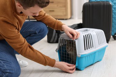 Evcil hayvanla seyahat et. Evde kedisi olan bir adam taşıyıcıyı kapatıyor.