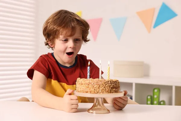 Cute boy with birthday cake at table indoors, space for text