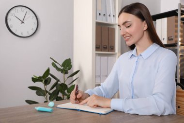 Ofisteki ahşap masada notlar alan mutlu bir kadın.