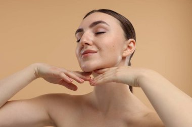 Güzel bir kadın bej arka planda çenesine dokunuyor.