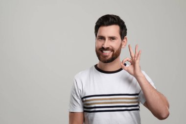 Sağlıklı temiz dişleri olan gülümseyen bir adamın portresi açık gri arka planda iyi bir jest gösteriyor. Metin için boşluk