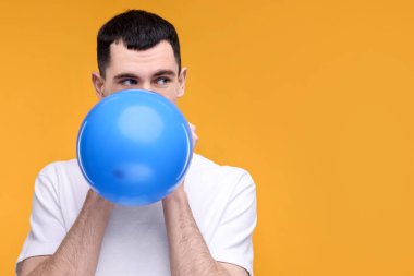 Sarı arka planda açık mavi balon şişiren genç adam. Metin için boşluk