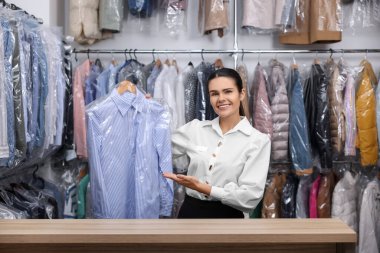 Kuru temizleme servisi. Kapalı mekanda elinde plastik torbayla askılık tutan mutlu işçi.