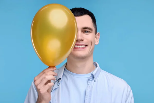 Happy young man with golden balloon on light blue background