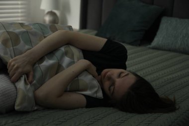 Üzgün genç kadın evde yatakta yatıyor.