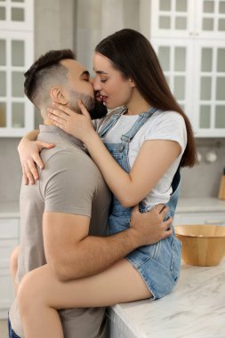 Şefkatli genç bir çift açık mutfakta öpüşüyor.