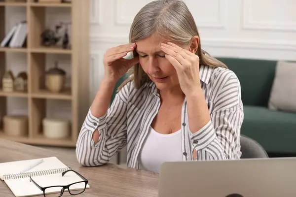 Menopause. Woman suffering from headache at wooden table indoors
