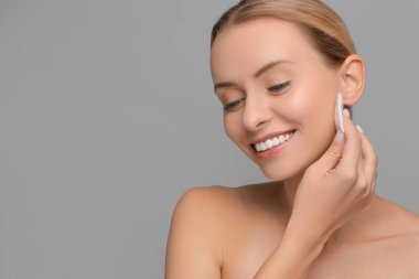 Gülümseyen kadın, gri arka planda pamuk yastıkla makyajı temizliyor. Metin için boşluk