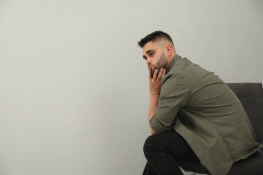 Üzgün adam açık gri duvarın yanında oturuyor. Metin için boşluk