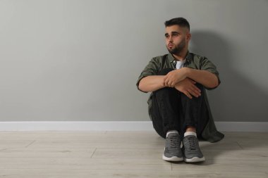 Açık gri duvarın yanında yerde oturan üzgün adam. Metin için boşluk