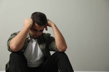 Üzgün adam açık gri duvarın yanında oturuyor. Metin için boşluk