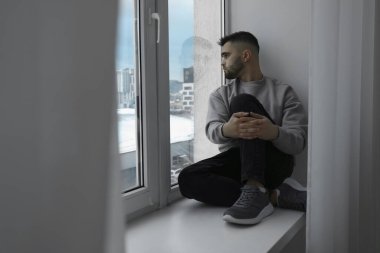 Üzgün adam pervazda oturuyor ve pencereye bakıyor.