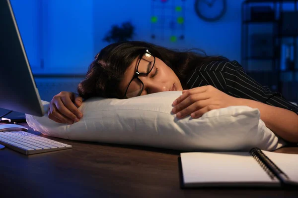 Tired overworked businesswoman napping with pillow at night in office