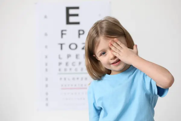 Little girl covering her eye against vision test chart