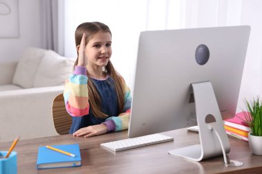 E-öğrenme. İçerideki masada çevrimiçi ders sırasında cevap vermek için elini kaldıran tatlı kız.