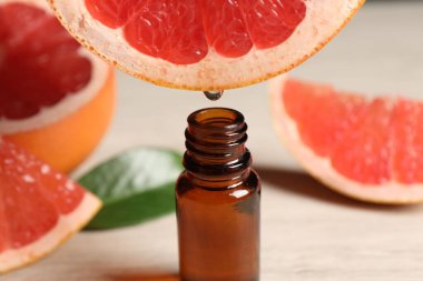 Temel yağ, arka planda hafif arkaplanda greyfurttan şişeye damlıyor.