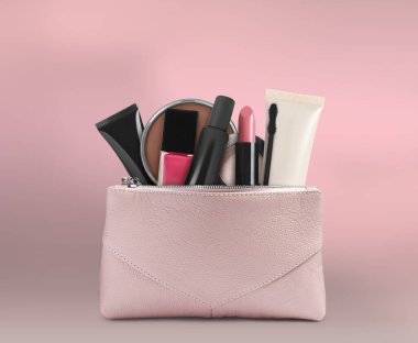 Pembe arka planda makyaj ürünleriyle dolu kozmetik çanta.