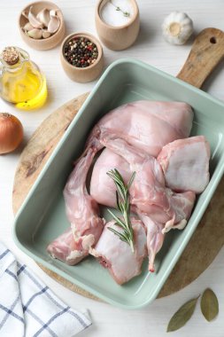 Pişirme kabında çiğ tavşan eti ve beyaz ahşap masa üzerinde ürünler.