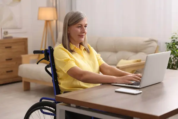 Woman in wheelchair using laptop at table in home office