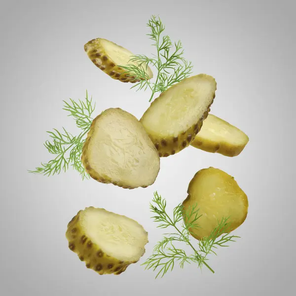 Slices of tasty pickled cucumbers and dill falling on light grey background