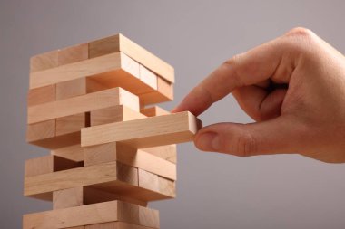 Jenga oynuyorum. Gri arkaplandaki tahta bloğu kuleden kaldıran adam, yakın plan