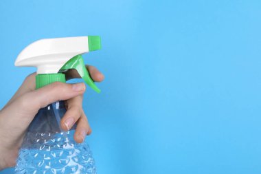 Açık mavi arka planda plastik sprey şişesi tutan kadın, yakın plan. Metin için boşluk