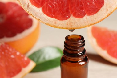 Temel yağ, arka planda hafif arkaplanda greyfurttan şişeye damlıyor.