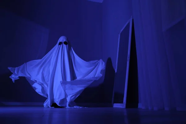 Creepy ghost. Woman covered with sheet in blue light, low angle view