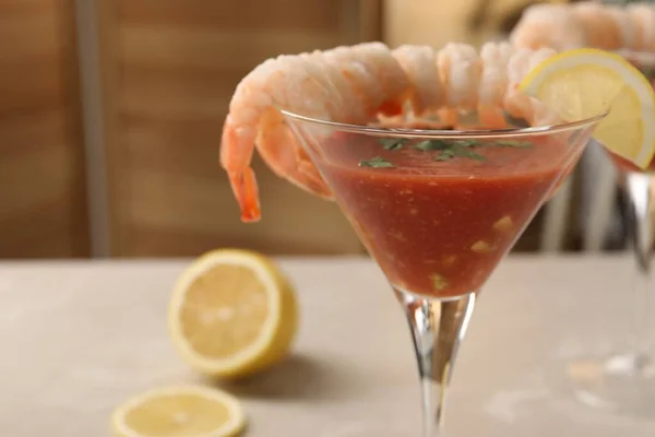 Tasty shrimp cocktail with sauce in glass and lemon on light table, closeup and space for text
