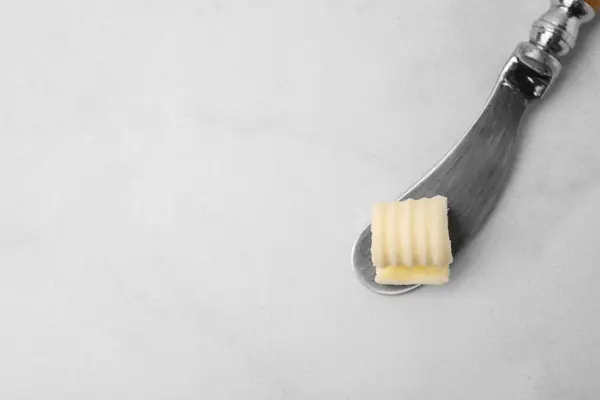 Tasty butter curl and knife on white table, top view. Space for text