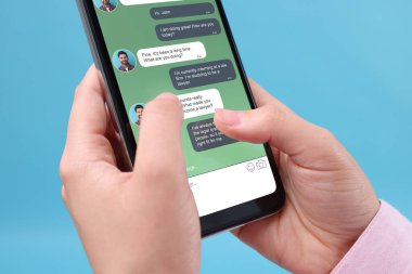 Arkadaşlarıyla mesajlaşan kadın akıllı telefondan açık mavi arkaplana mesaj uygulaması kullanıyor, yakın plan