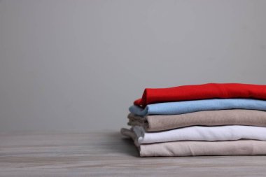 Sıralama ve düzenleme. Aydınlık ahşap masada katlanmış farklı kıyafetlerin yığını, yakın plan. Metin için boşluk